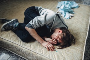 Male drug addict with syringe in hand sleeping in bed after dose. Addiction concept, narcotic addicted people